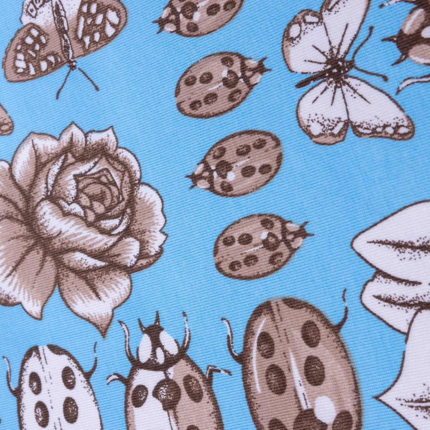 A close up of stretch jersey fabric featuring sketches of beetles, butterflies, florals and bugs on a light blue bright background