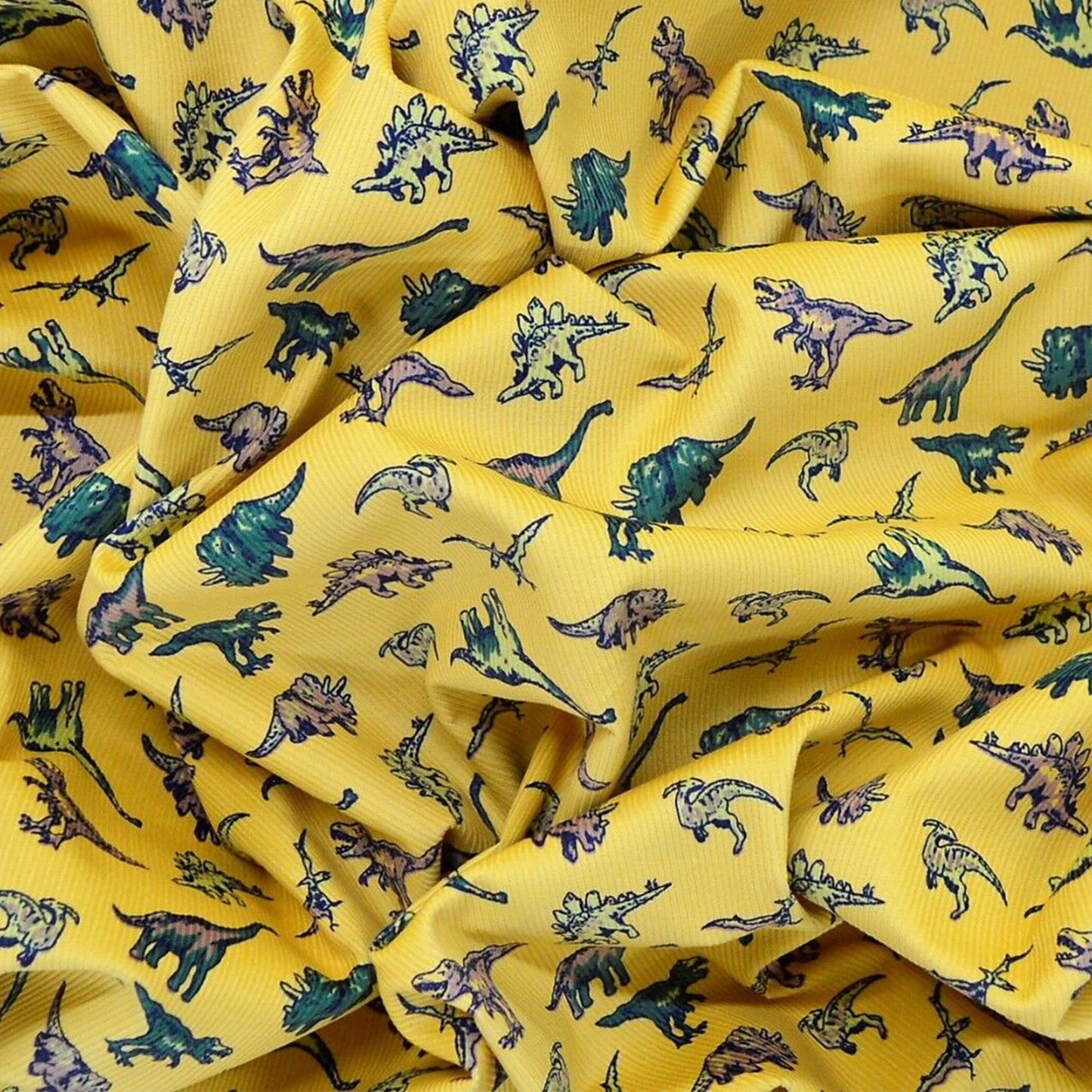 A crumpled up look at the stretch gold mustard coloured dinosaur corduroy fabric with different dinos great for children's clothing, sewing and homeware projects