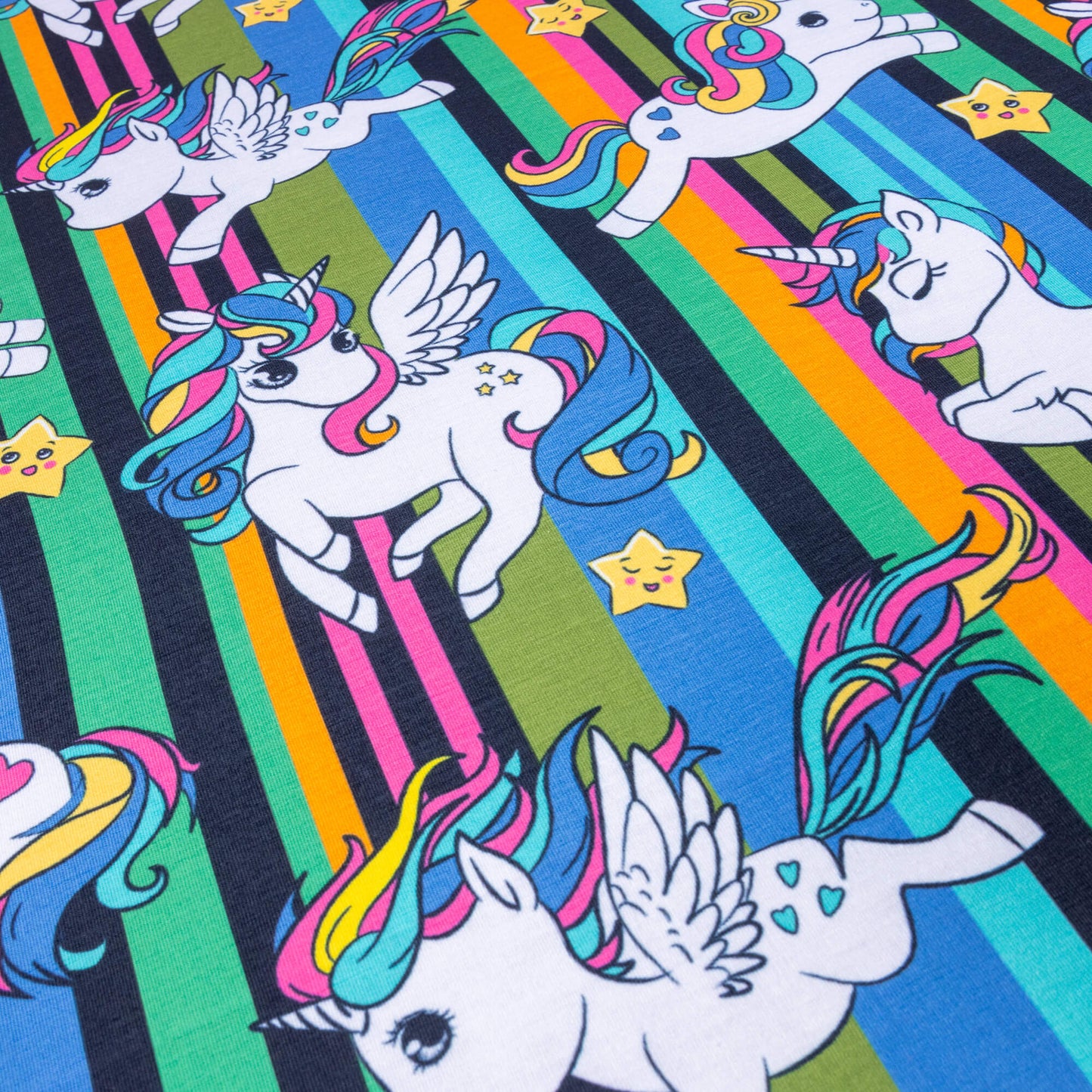 A look at Jersey fabric featuring unicorns and flying unicorns with pink, blue and yellow flowing hair against a background of pink, blue, yellow, green and black stripes. There are also cute smiley stars