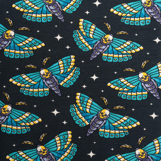 Dark fabric adorned with a vibrant pattern of moths and stars. The moths are illustrated with blue and yellow wings, and their bodies feature a whimsical skull design. The background includes small star motifs, enhancing the enchanting design