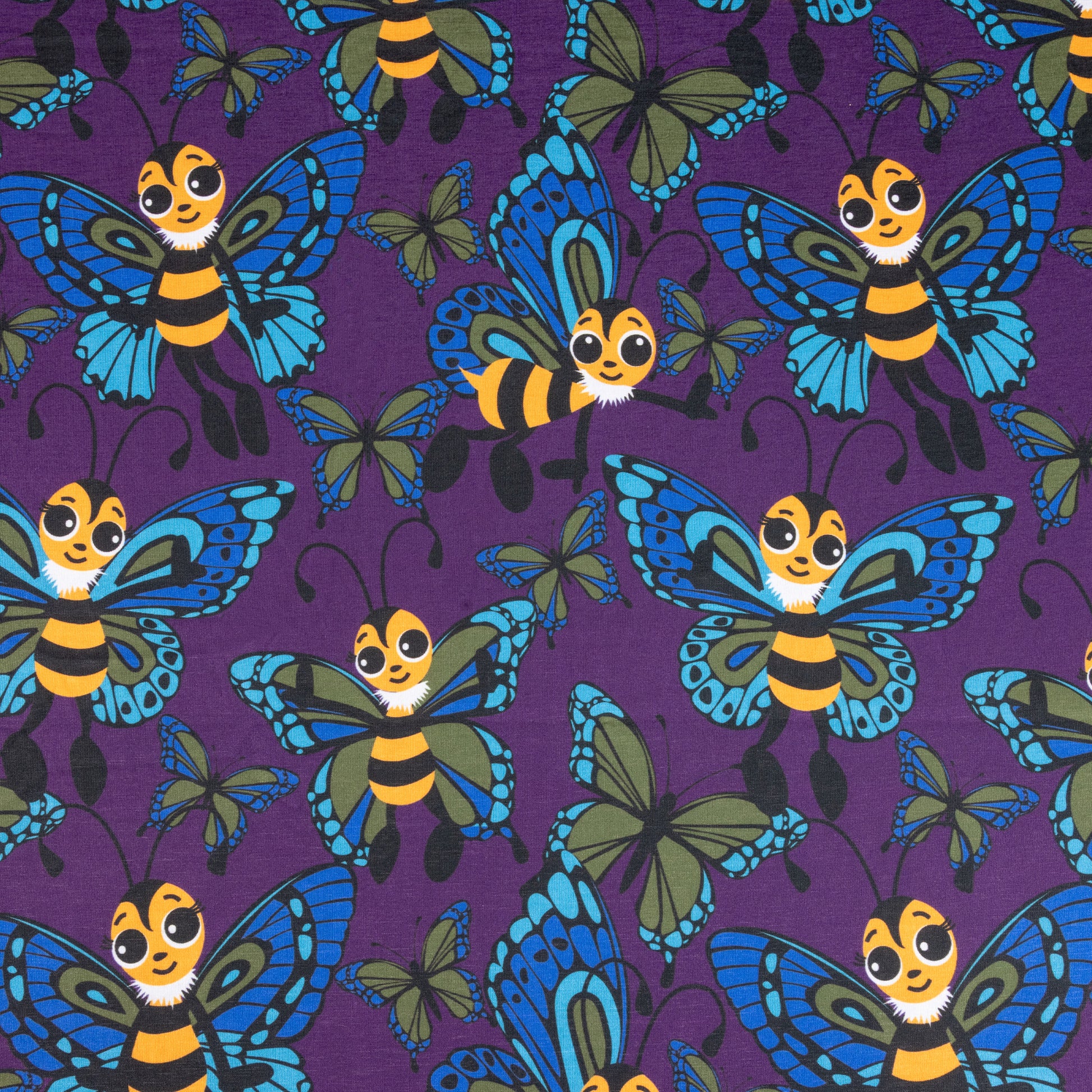 A fabric showing cute cartoon bees with butterfly wings. The bees are yellow and black with eyelashes, their wings are blue and green. They are against a purple background with various sized butterflies too.