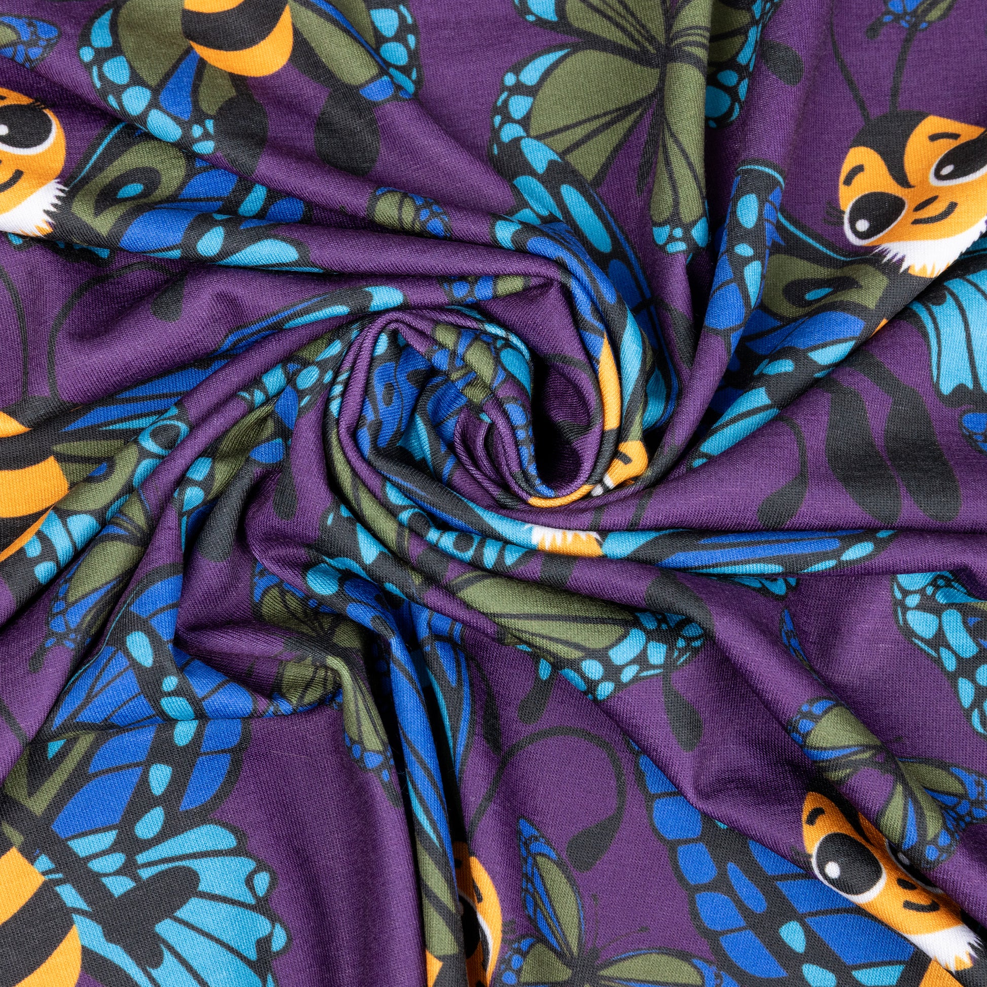 A swirl of fabric showing cute cartoon bees with butterfly wings. The bees are yellow and black with eyelashes, their wings are blue and green. They are against a purple background with various sized butterflies too.