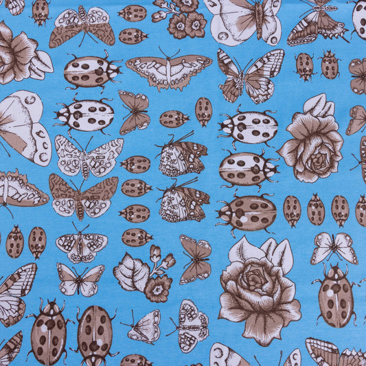 A wide picture of stretch jersey fabric featuring sketches of beetles, butterflies, florals and bugs on a light blue bright background