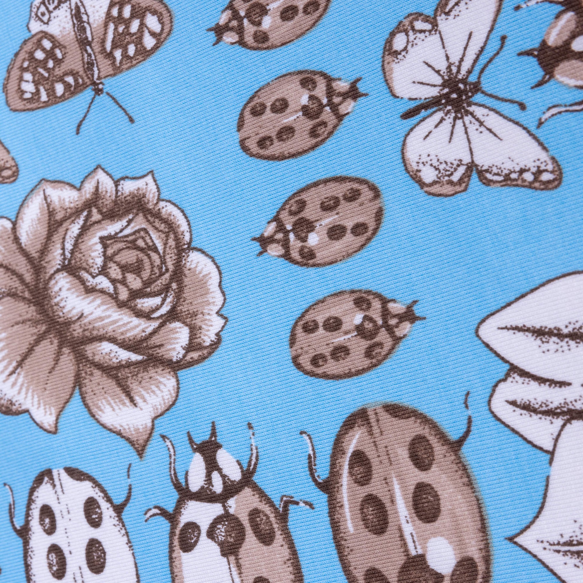A close up of stretch jersey fabric featuring sketches of beetles, butterflies, florals and bugs on a light blue bright background
