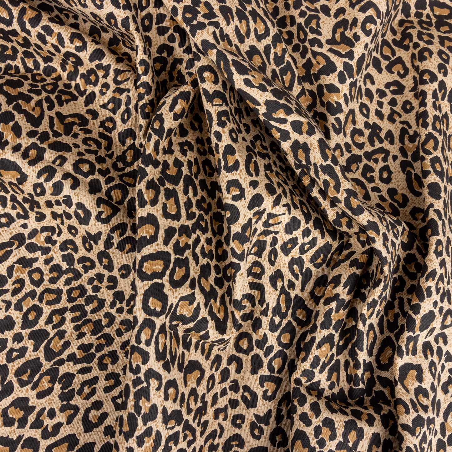A close up of brown leopard print fabric with black, beige and a soft beige background the tones are warm the fabric is crumpled